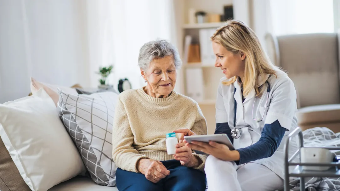 A professional social care specialist sitting with an elderly client in a home setting, representing the trusted, person-centred mental capacity assessments provided by Nellie Supports across the UK.