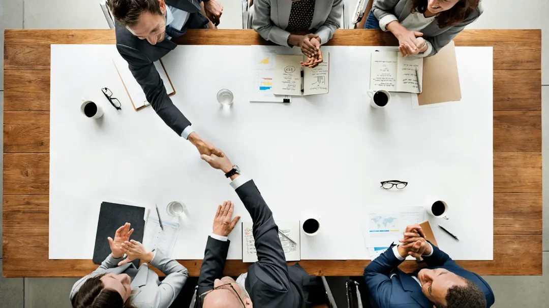 An overhead view of business professionals shaking hands over a boardroom table, representing strategic B2B partnerships and successful lead generation.