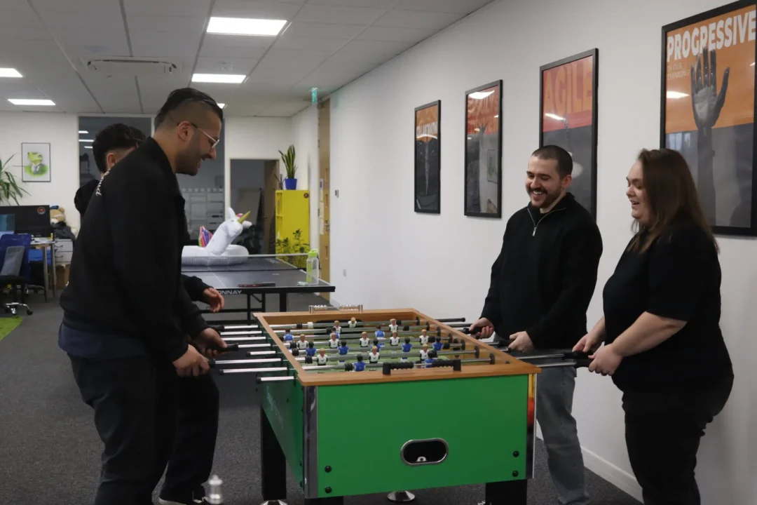 Four members of the Repeat Digital team laughing while playing a game of table football in their Nottingham office.