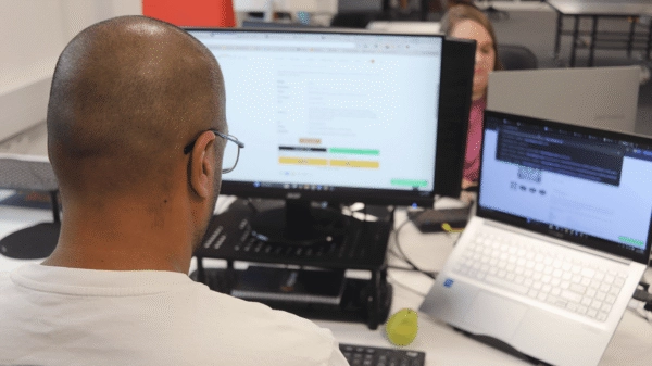 A digital marketing specialist at Repeat Digital working at a desk with a laptop and a large desktop monitor displaying website data and campaign performance.