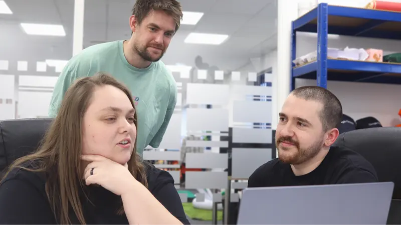 Three members of the Repeat Digital team collaborating and discussing a project over a laptop in their Nottingham office.