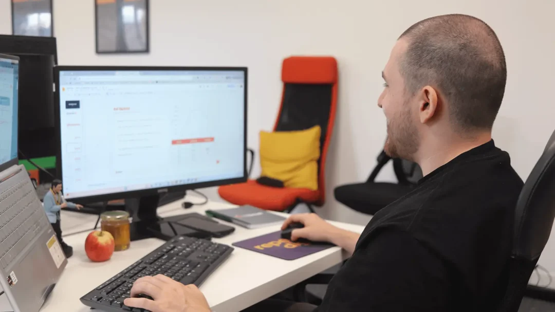 A digital marketing specialist reviewing data charts and ad spend on a computer monitor at a white desk.